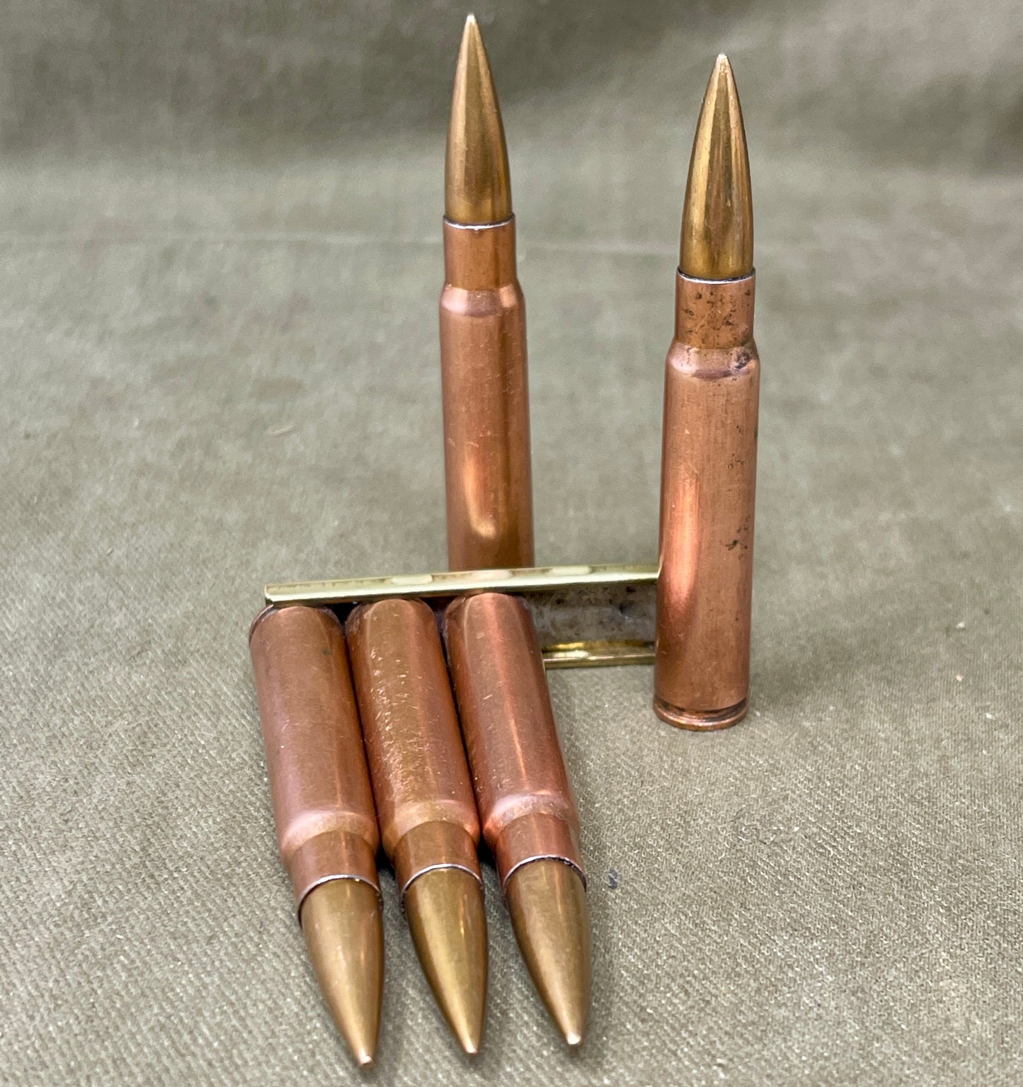 Five rifle cartridges with brass casings on a textured surface
