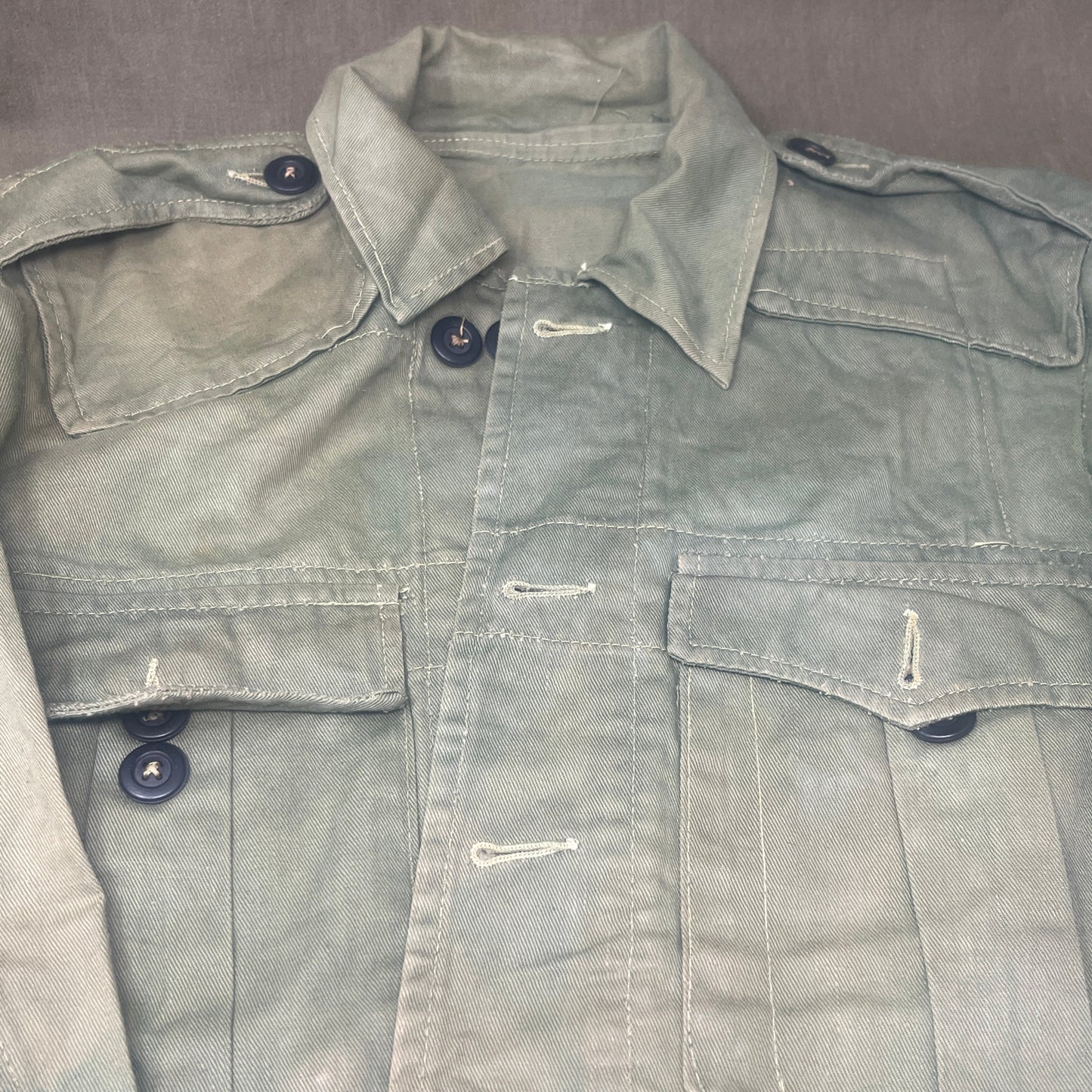 This original 1951-dated British Army Jungle Green Bush Jacket is a superb example of early post-war tropical combat clothing, manufactured by the reputable N. Lotery & Co. Ltd. Made from sturdy, breathable cotton in classic Jungle Green, this jacket was designed for use in humid and challenging environments such as Malaya and other post-war theatres of operation.
The jacket is in excellent condition, showing minimal signs of wear, with its color, stitching, and structural integrity all remarkably well-pre