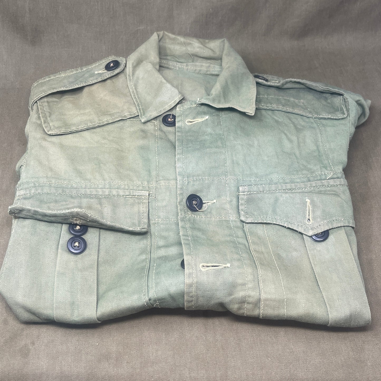 This original 1951-dated British Army Jungle Green Bush Jacket is a superb example of early post-war tropical combat clothing, manufactured by the reputable N. Lotery & Co. Ltd. Made from sturdy, breathable cotton in classic Jungle Green, this jacket was designed for use in humid and challenging environments such as Malaya and other post-war theatres of operation.
The jacket is in excellent condition, showing minimal signs of wear, with its color, stitching, and structural integrity all remarkably well-pre