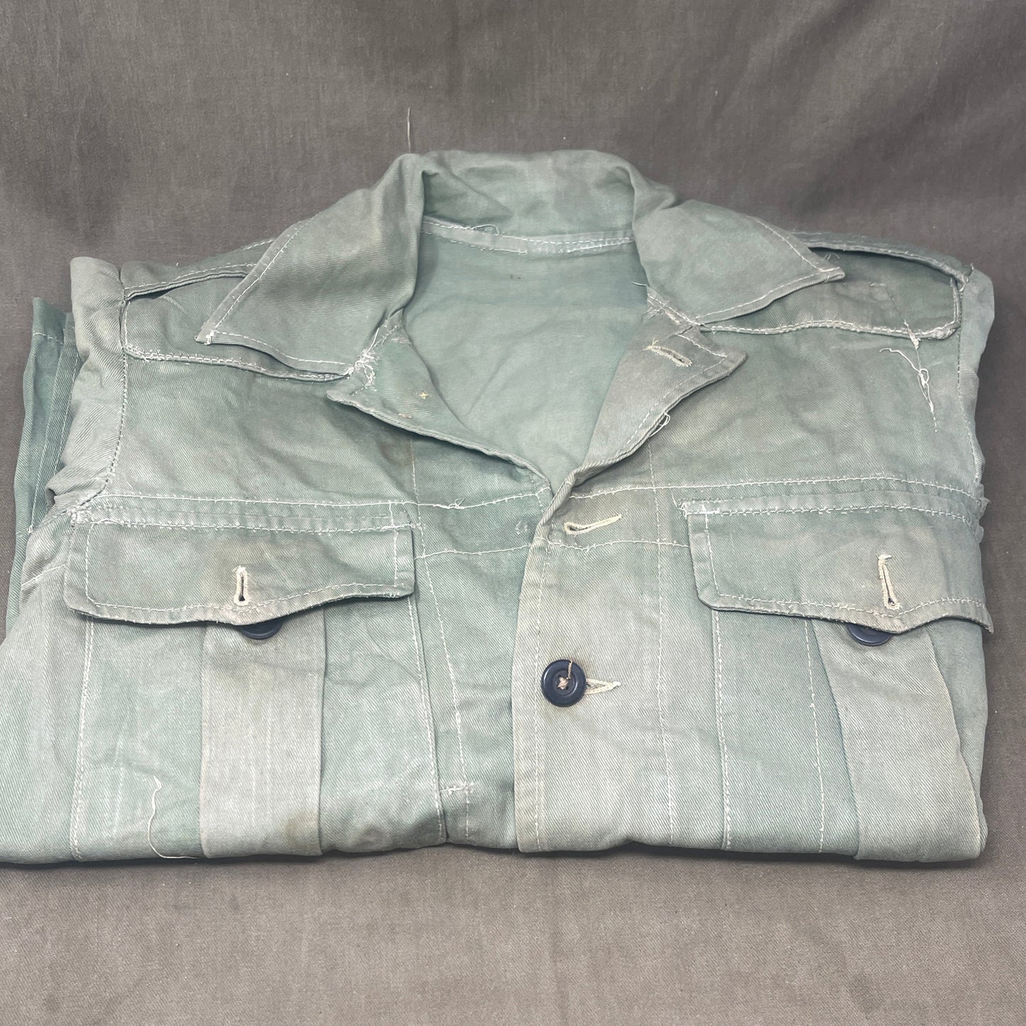This original 1951-dated British Army Jungle Green Bush Jacket is a superb example of early post-war tropical combat clothing, manufactured by the reputable N. Lotery & Co. Ltd. Made from sturdy, breathable cotton in classic Jungle Green, this jacket was designed for use in humid and challenging environments such as Malaya and other post-war theatres of operation.
The jacket is in excellent condition, showing minimal signs of wear, with its color, stitching, and structural integrity all remarkably well-pre