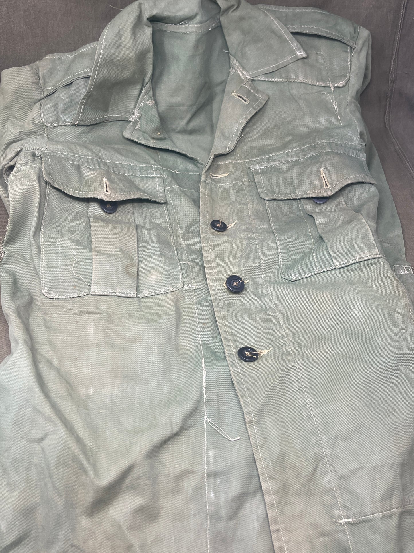 This original 1951-dated British Army Jungle Green Bush Jacket is a superb example of early post-war tropical combat clothing, manufactured by the reputable N. Lotery & Co. Ltd. Made from sturdy, breathable cotton in classic Jungle Green, this jacket was designed for use in humid and challenging environments such as Malaya and other post-war theatres of operation.
The jacket is in excellent condition, showing minimal signs of wear, with its color, stitching, and structural integrity all remarkably well-pre