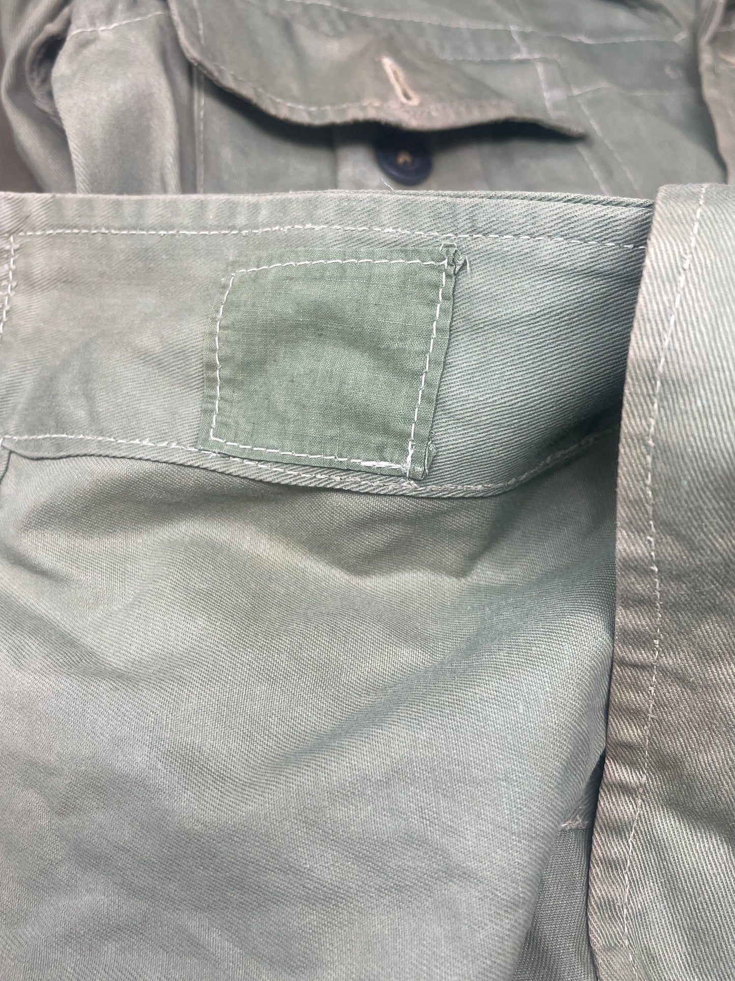 This original 1951-dated British Army Jungle Green Bush Jacket is a superb example of early post-war tropical combat clothing, manufactured by the reputable N. Lotery & Co. Ltd. Made from sturdy, breathable cotton in classic Jungle Green, this jacket was designed for use in humid and challenging environments such as Malaya and other post-war theatres of operation.
The jacket is in excellent condition, showing minimal signs of wear, with its color, stitching, and structural integrity all remarkably well-pre