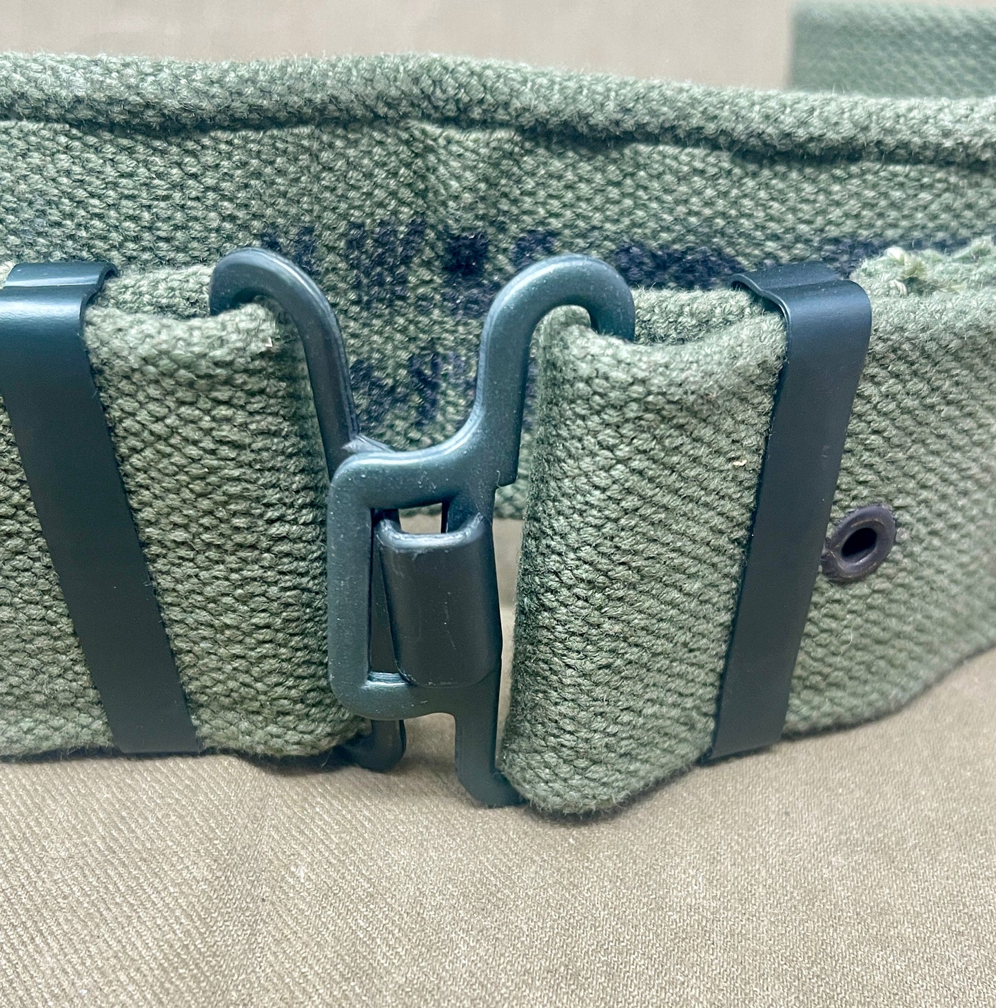 Green woven belt with a metal buckle on a beige surface