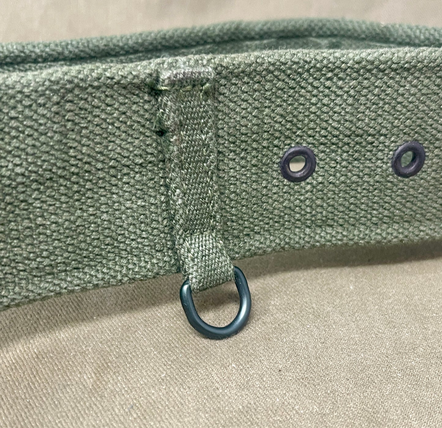 Close-up of a green belt with metal rings on a beige background