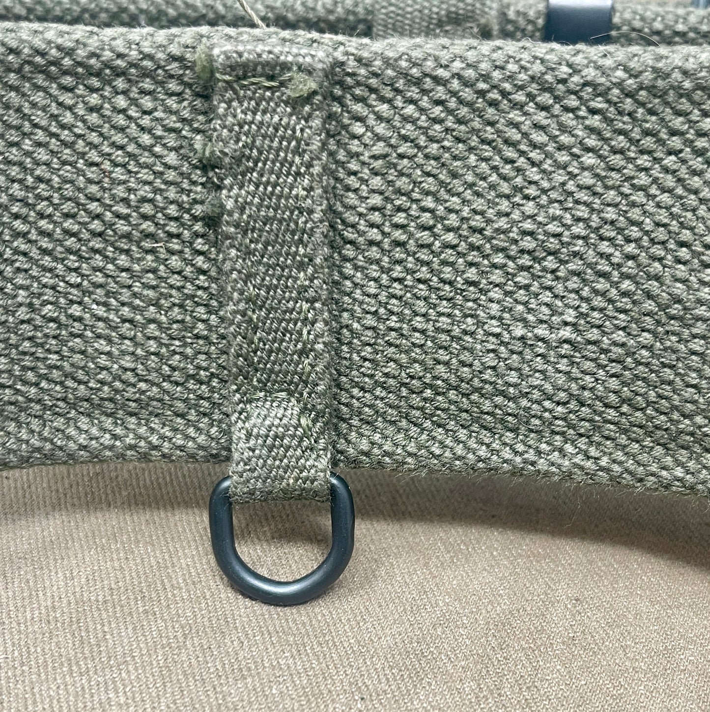 Close-up of a textured fabric surface with a metal ring attached, on a beige background.