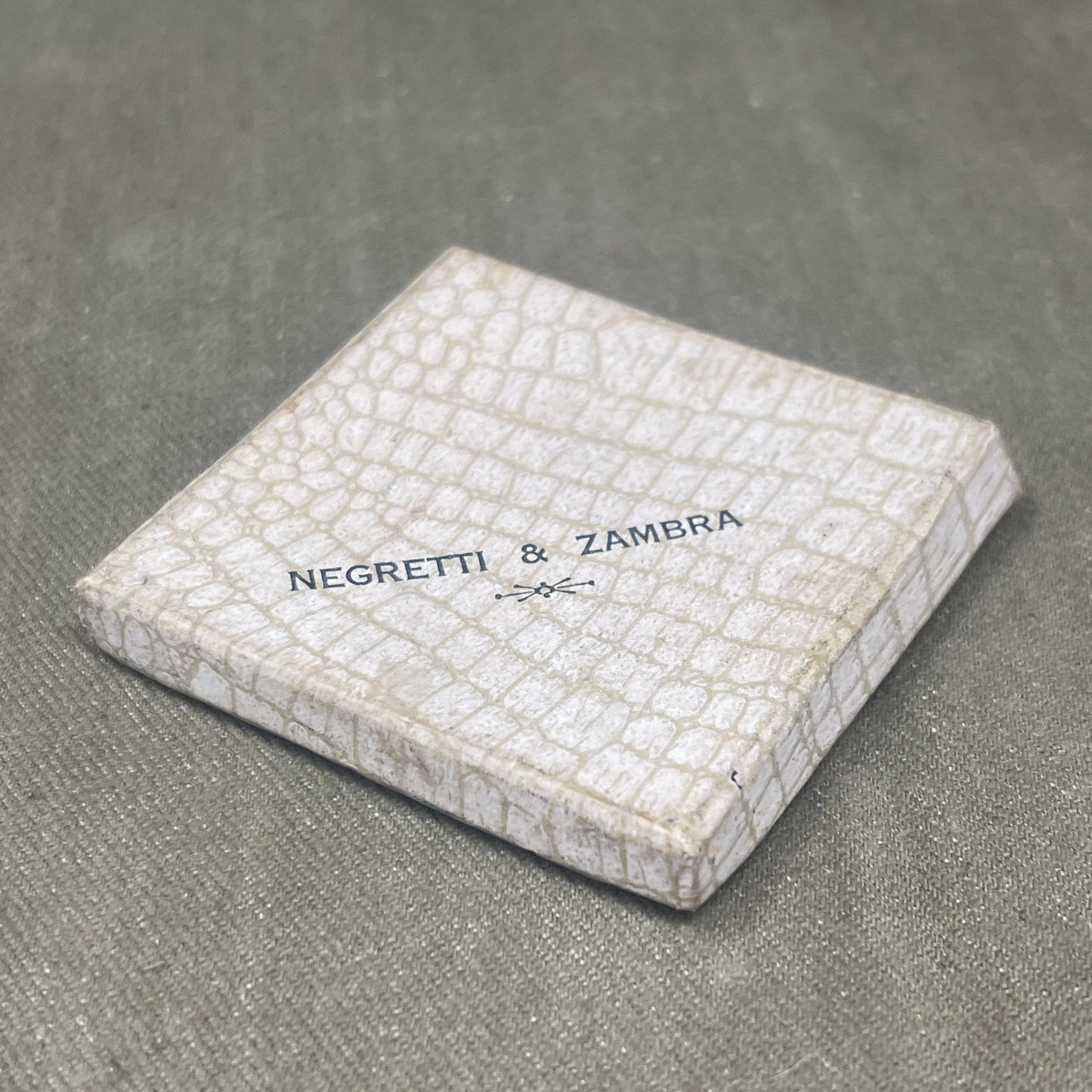 White textured wallet with 'Negretti & Zambra' branding on a gray surface