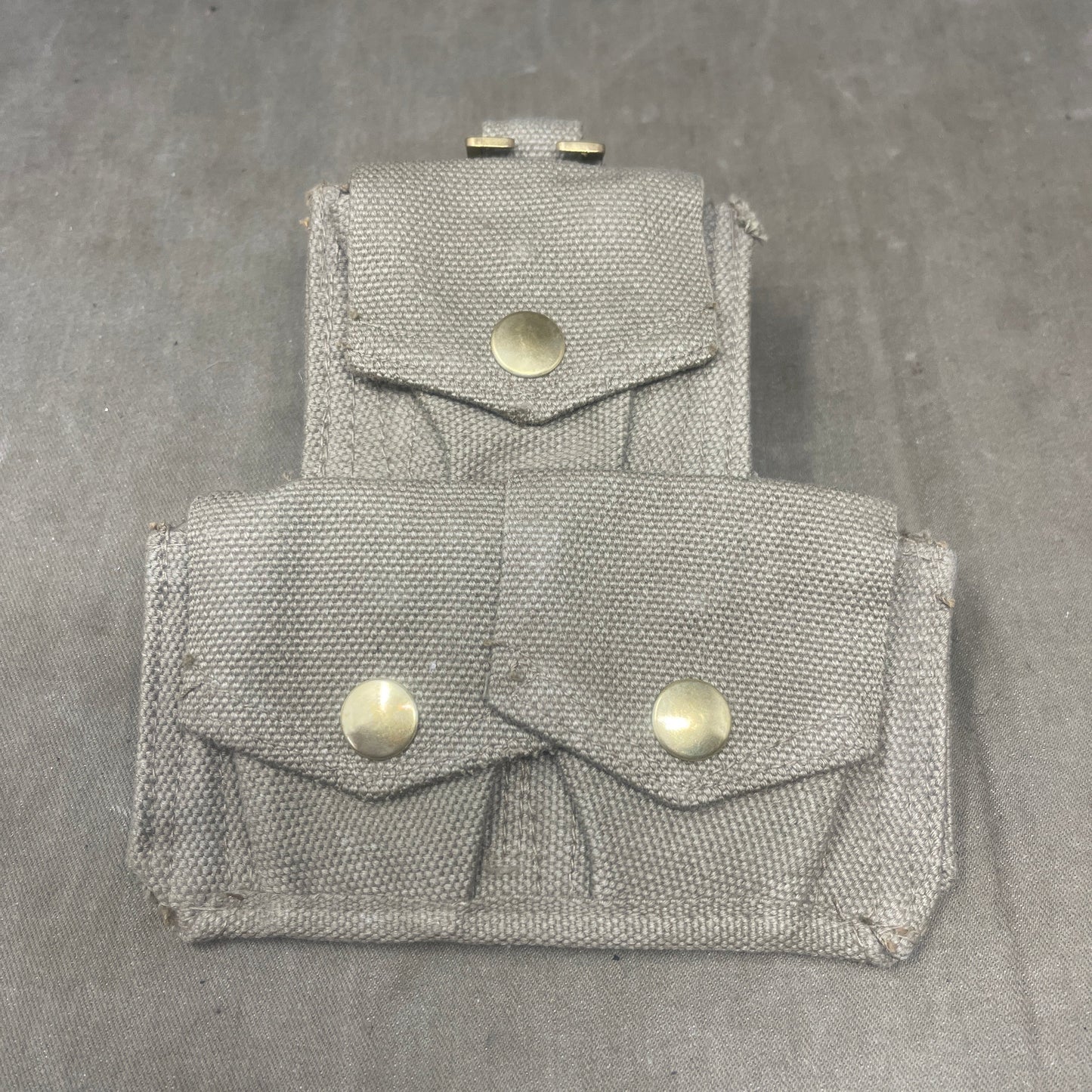 Two gray fabric pouches with buttons on a gray surface