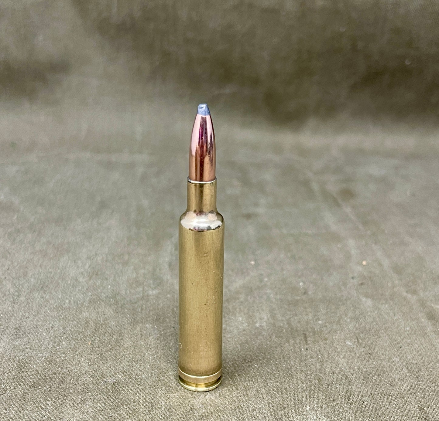 Bronze-colored rifle cartridge on a textured beige background