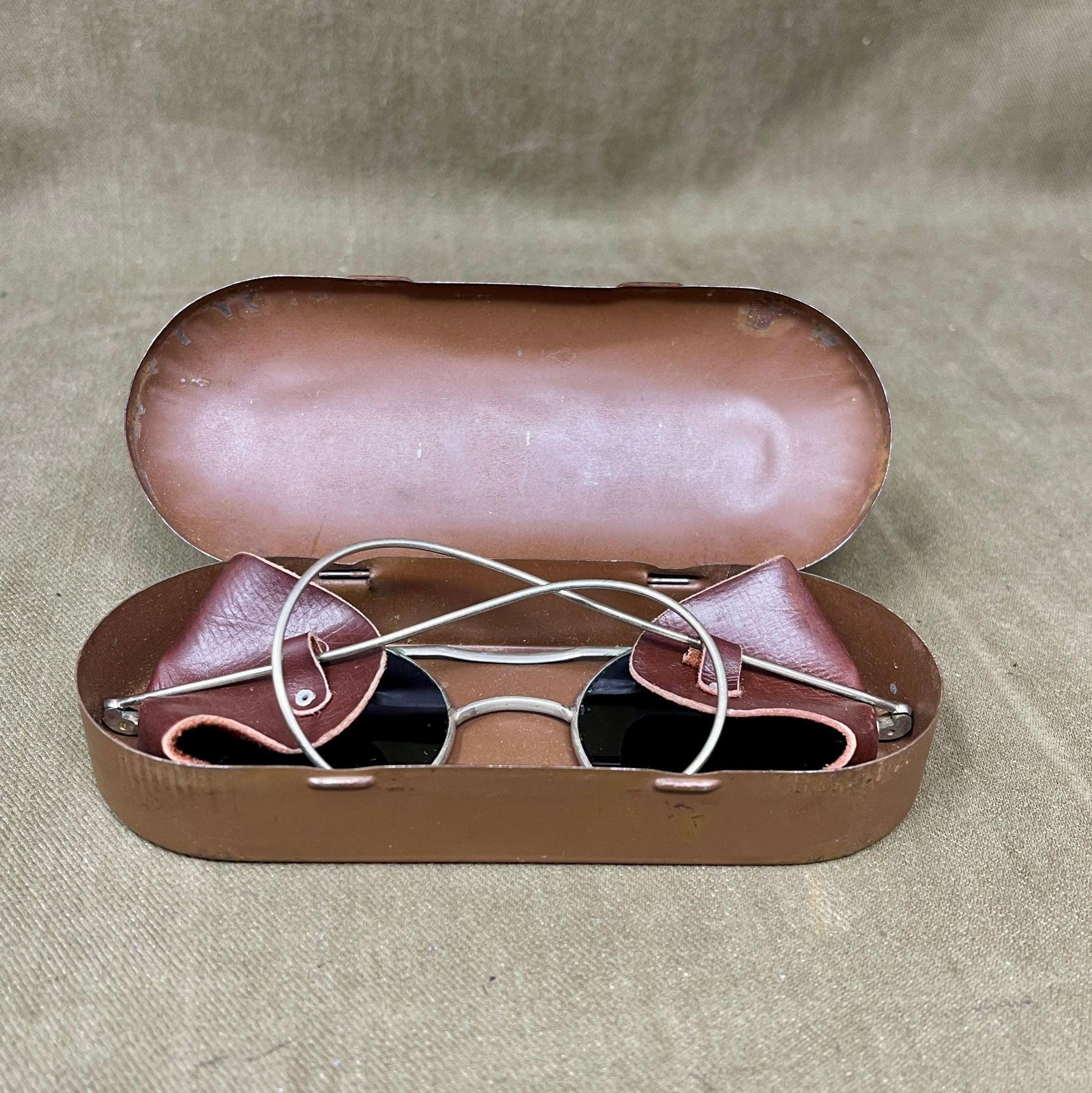 Brown sunglasses in an open brown case on a beige fabric background
