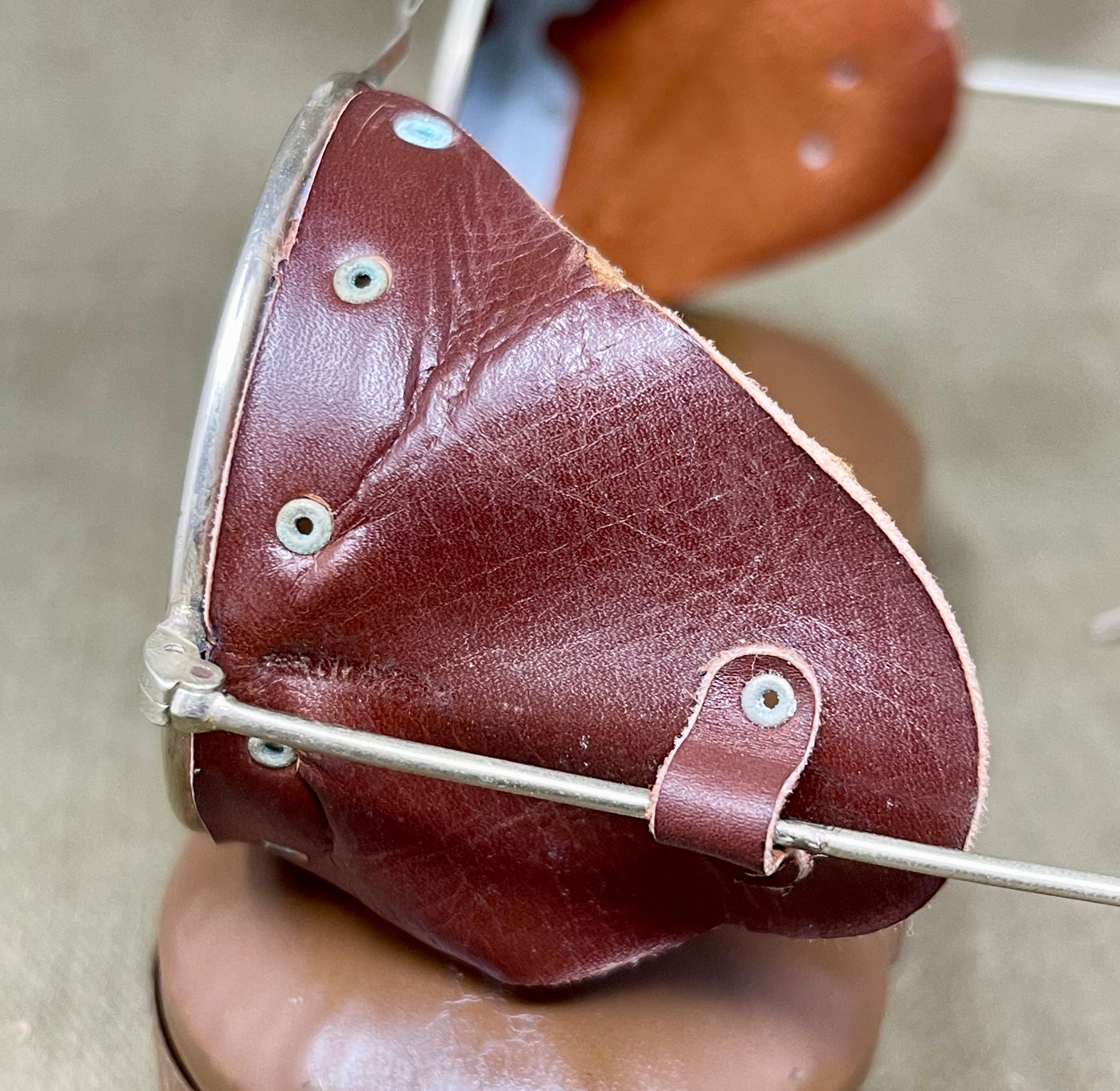 Brown leather patch with silver metal frame held by a hand against a neutral background