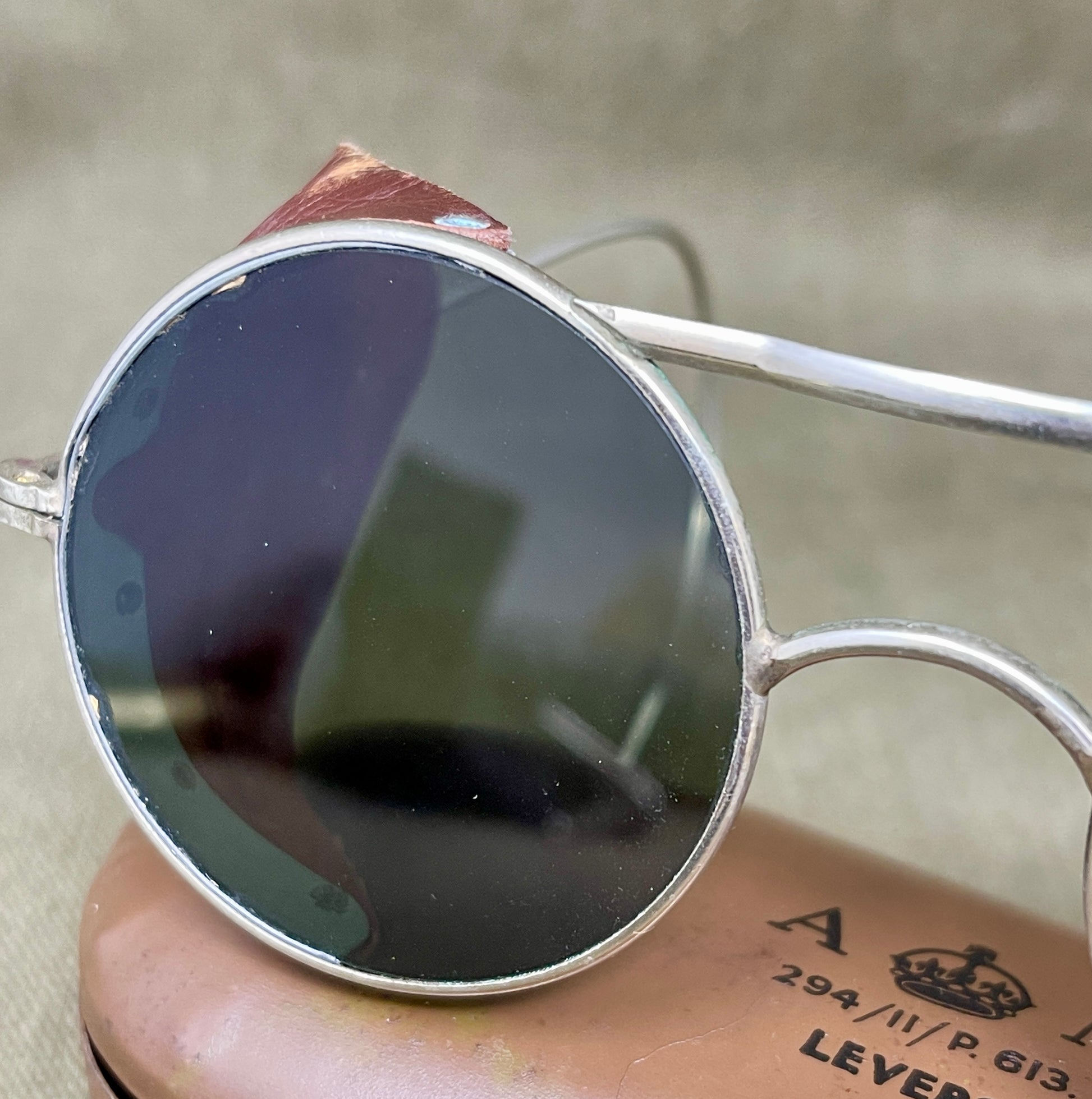 Round sunglasses with silver frame held by a person with tattoos.