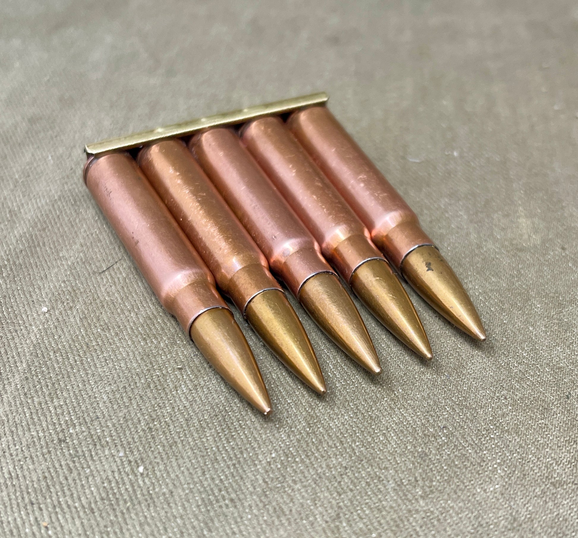 Five rifle bullets in a brass holder on a textured surface