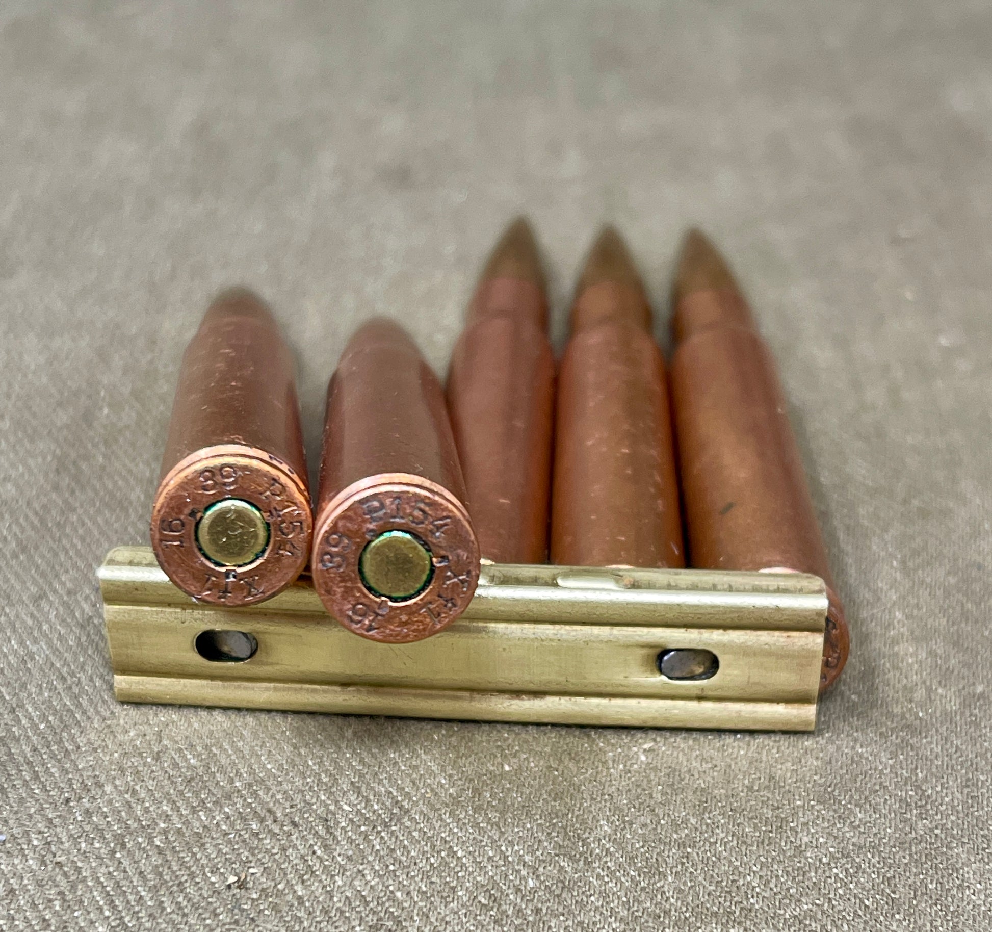 Five rifle cartridges on a metal holder against a textured gray background