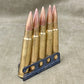 Five rifle bullets on a holder against a neutral background