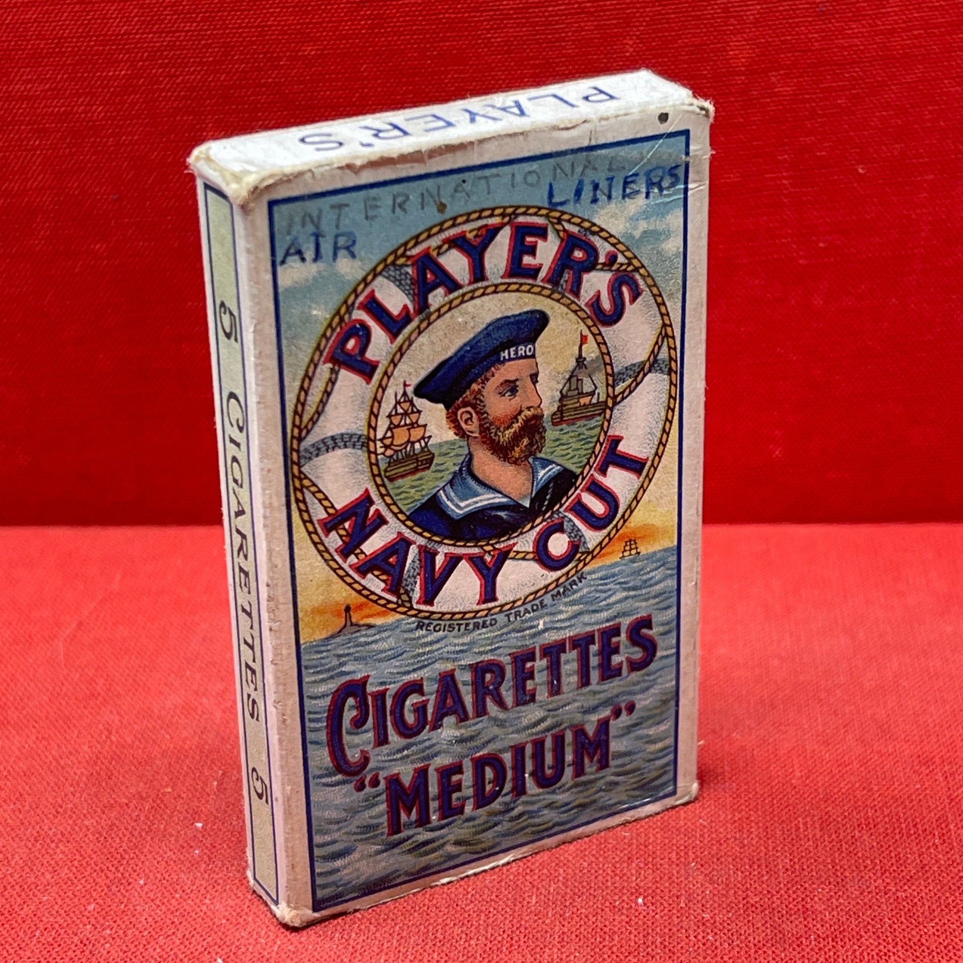 An empty packet for 10 Player's Medium Navy Cut cigarettes. The front has an ocean scene and a sailor framed in a life belt.