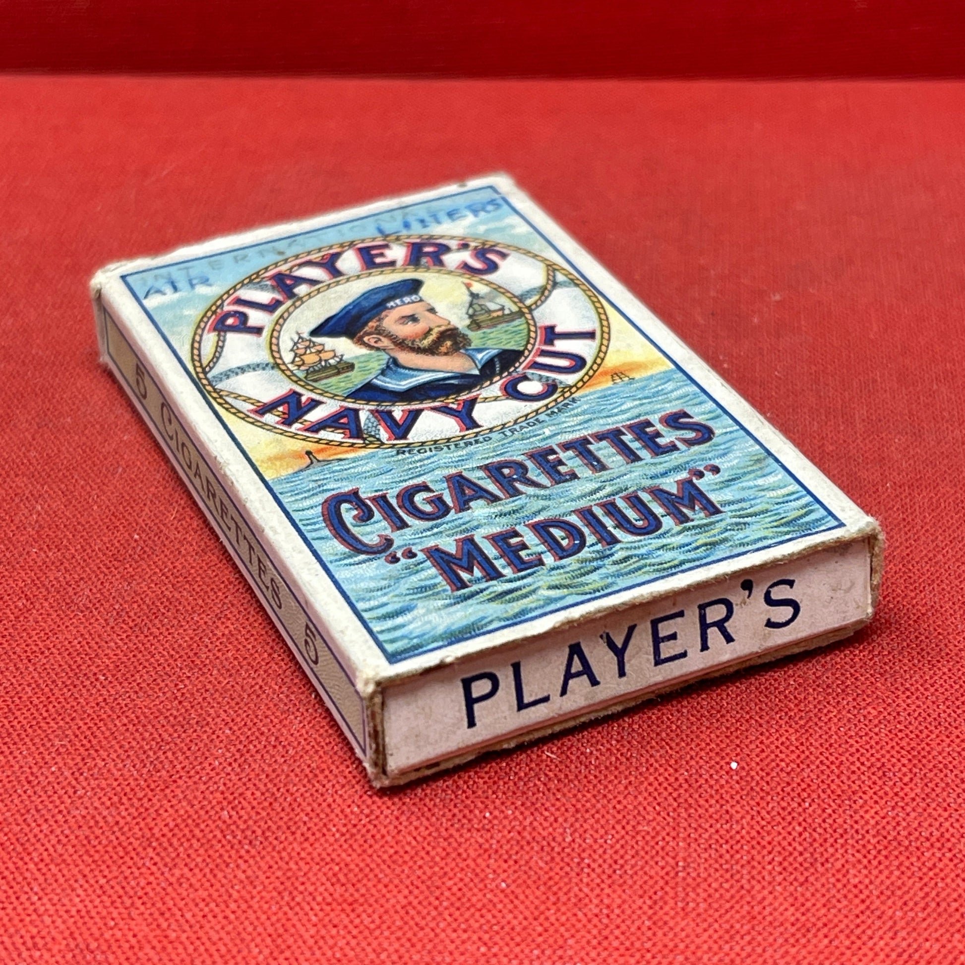 An empty packet for 10 Player's Medium Navy Cut cigarettes. The front has an ocean scene and a sailor framed in a life belt.