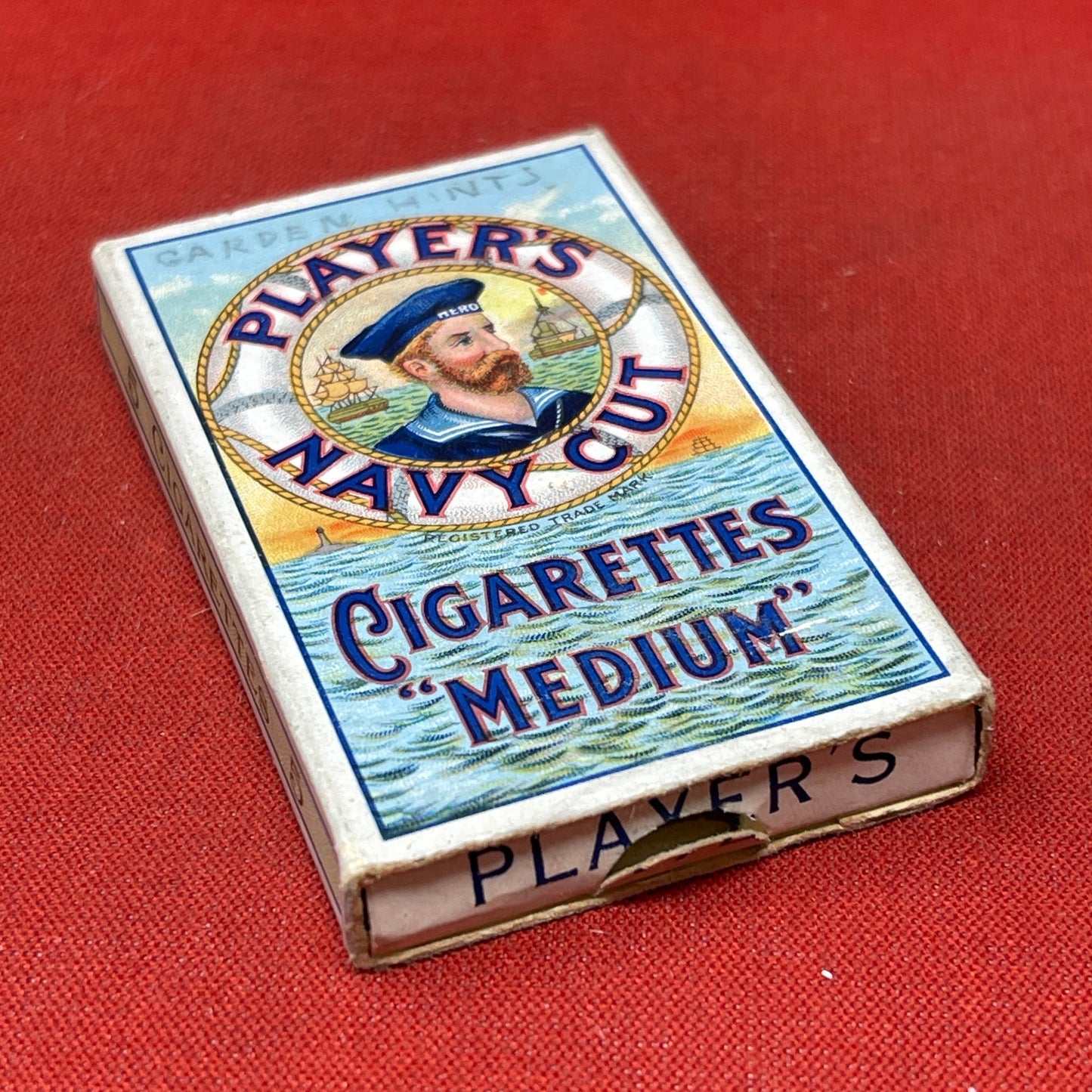 An empty packet for 10 Player's Medium Navy Cut cigarettes. The front has an ocean scene and a sailor framed in a life belt.