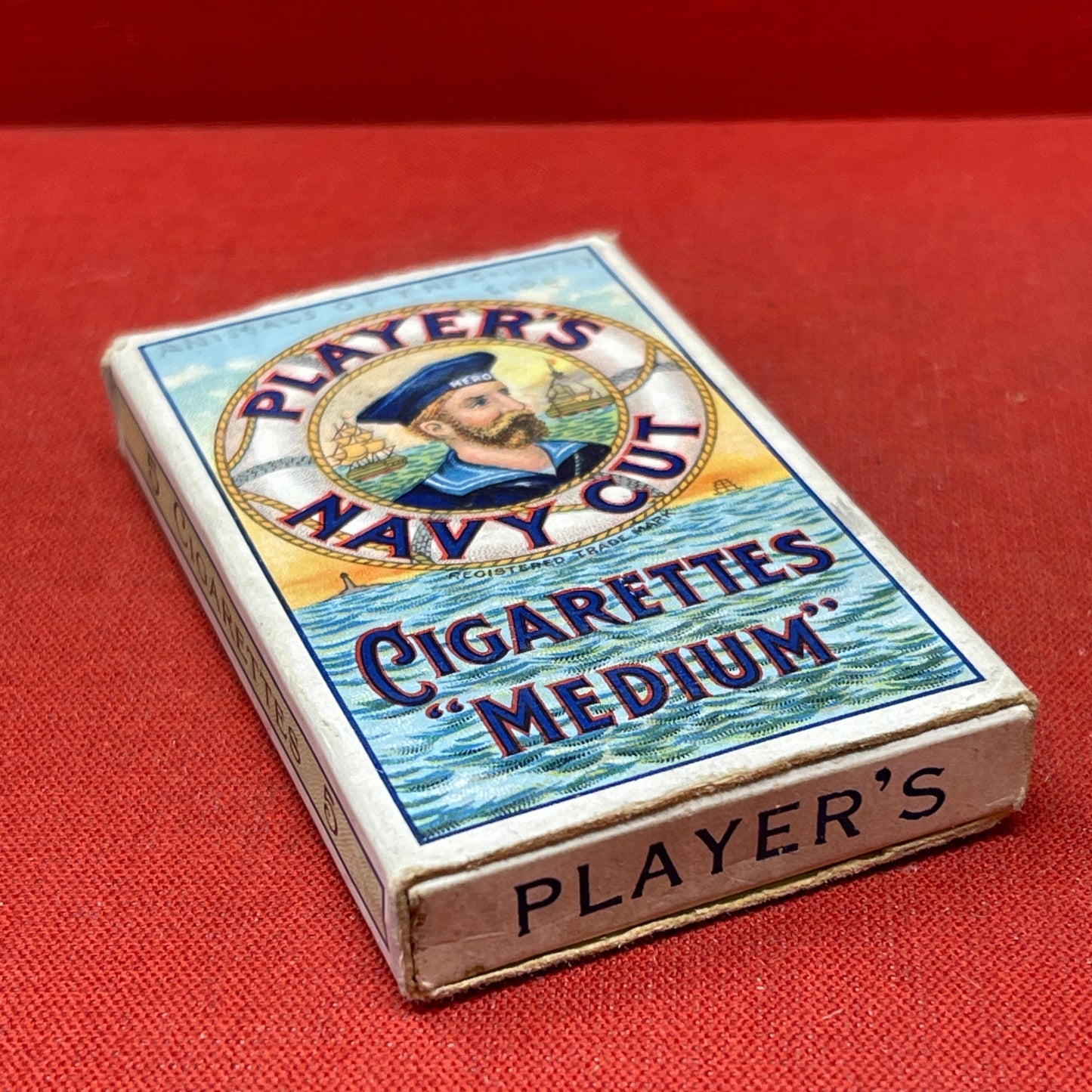 An empty packet for 10 Player's Medium Navy Cut cigarettes. The front has an ocean scene and a sailor framed in a life belt.