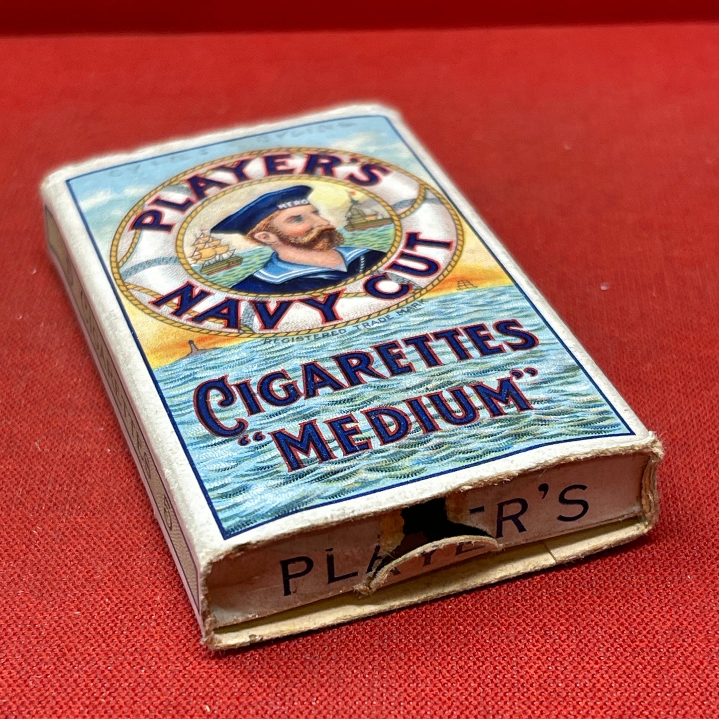 An empty packet for 10 Player's Medium Navy Cut cigarettes. The front has an ocean scene and a sailor framed in a life belt.