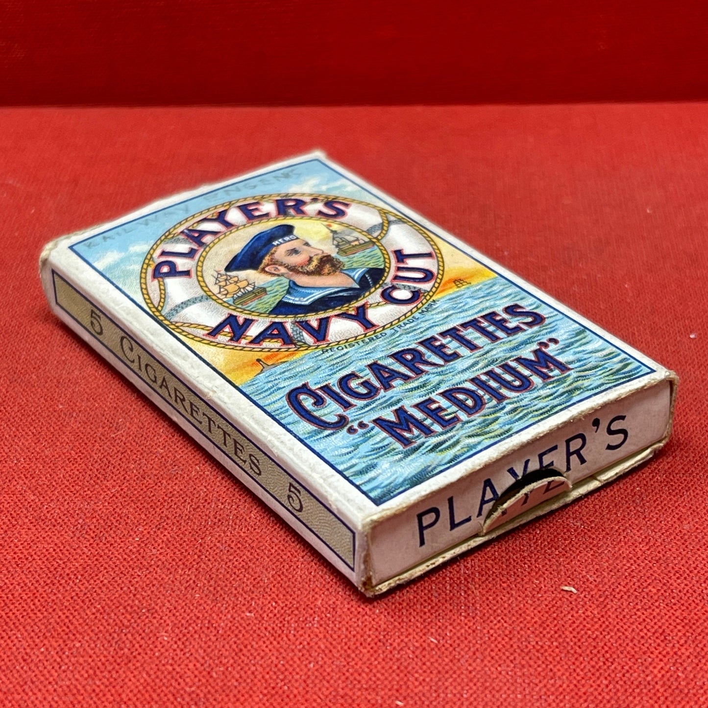 An empty packet for 10 Player's Medium Navy Cut cigarettes. The front has an ocean scene and a sailor framed in a life belt.