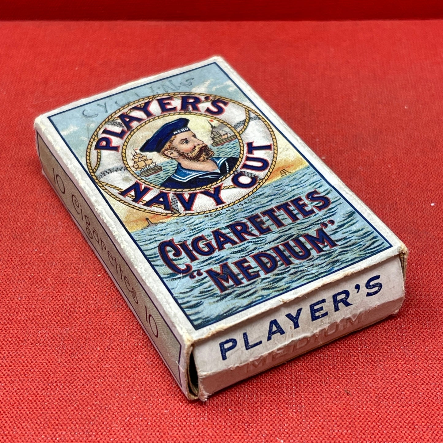 An empty packet for 10 Player's Medium Navy Cut cigarettes. The front has an ocean scene and a sailor framed in a life belt.