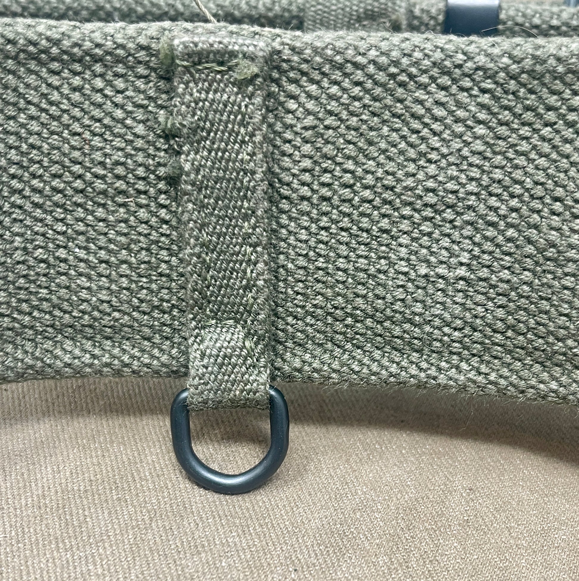 Close-up of a textured fabric surface with a metal ring attached, on a beige background.
