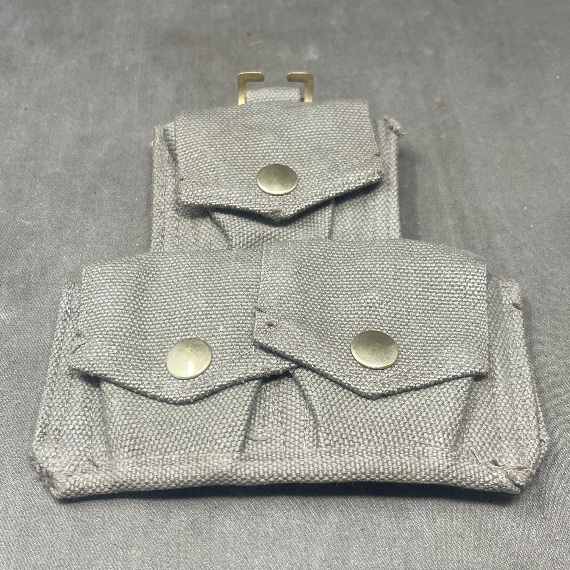 Folded fabric pouch with metal buttons on a gray background