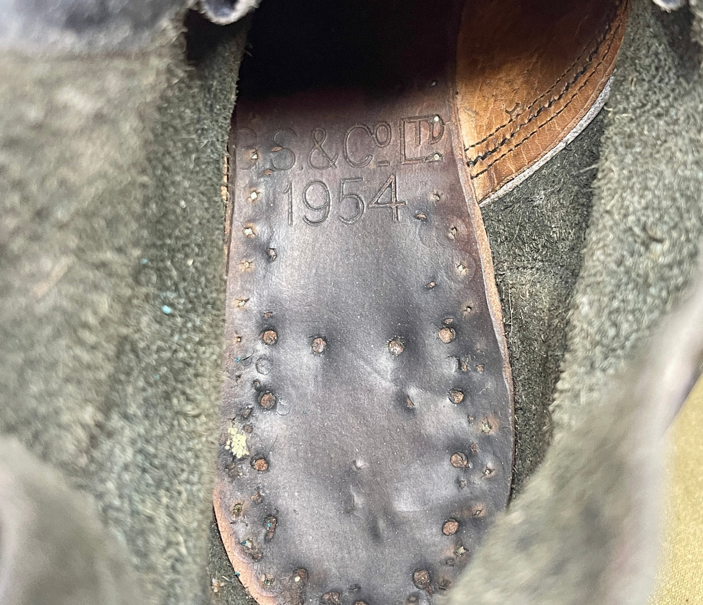 Close-up of a shoe sole with 'B.S.C. & Co.' and '1954' embossed on it, set against a textured green background.
