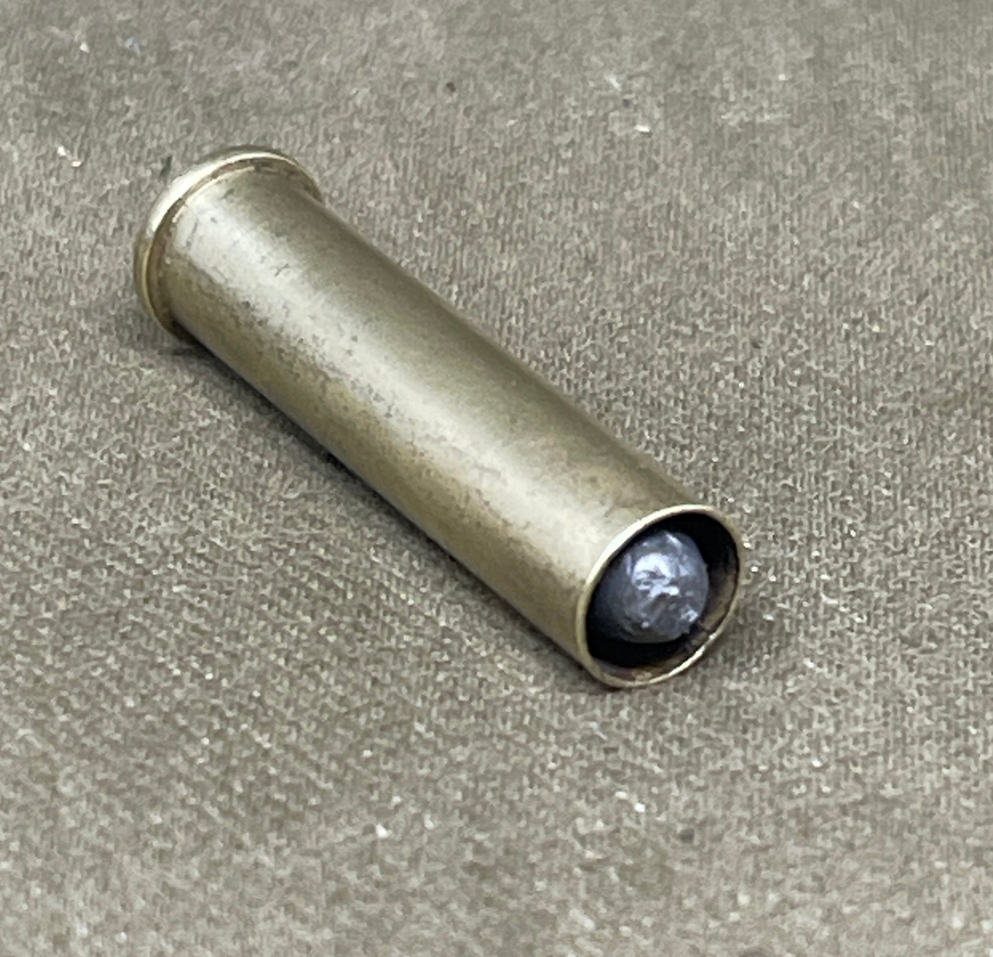 Metallic cylindrical object with a dark gray sphere inside on a textured beige surface
