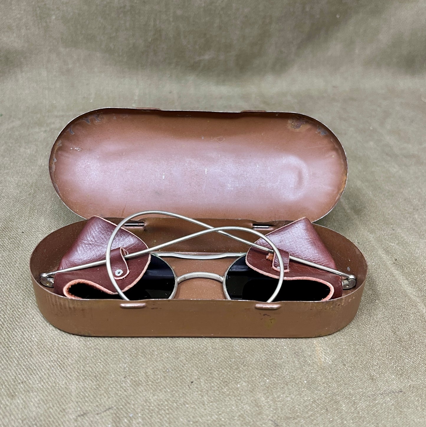 Brown sunglasses in an open brown case on a beige fabric background