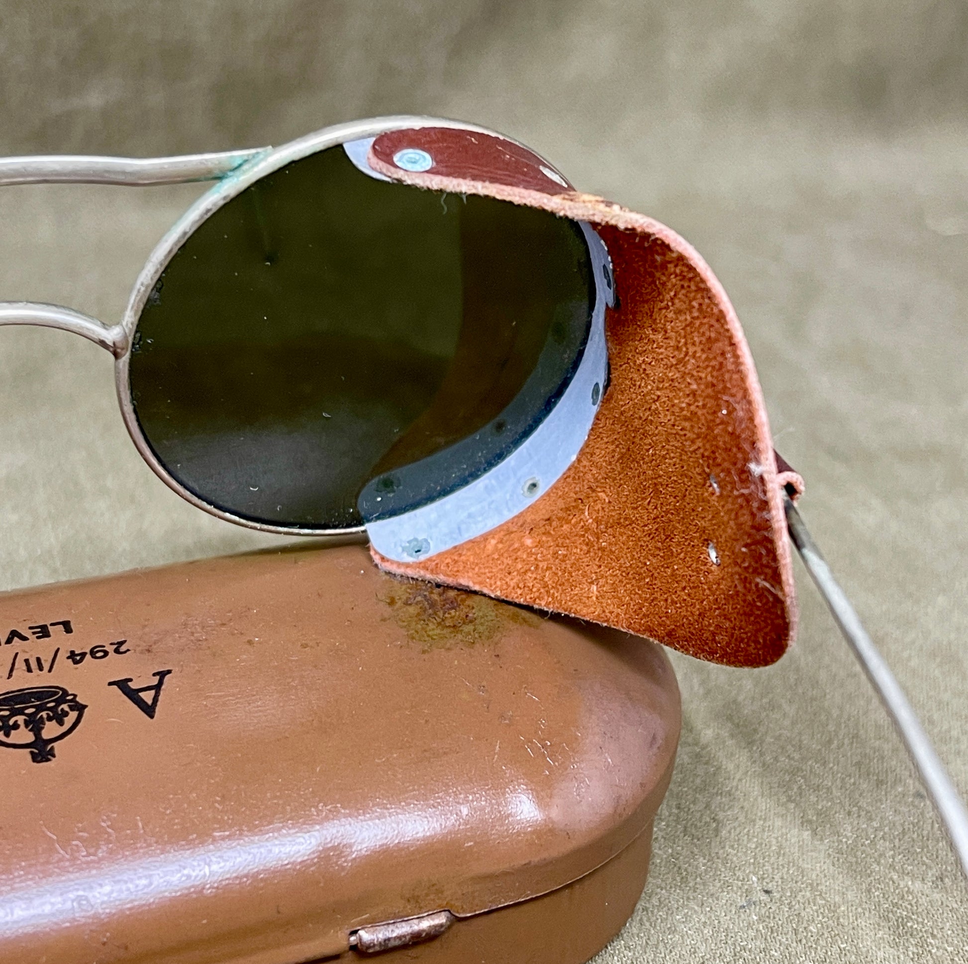 Aviator sunglasses with brown leather case on a beige background