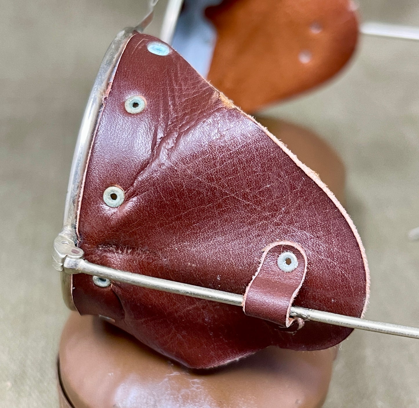 Brown leather patch with silver metal frame held by a hand against a neutral background