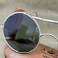 Round sunglasses with silver frame held by a person with tattoos.